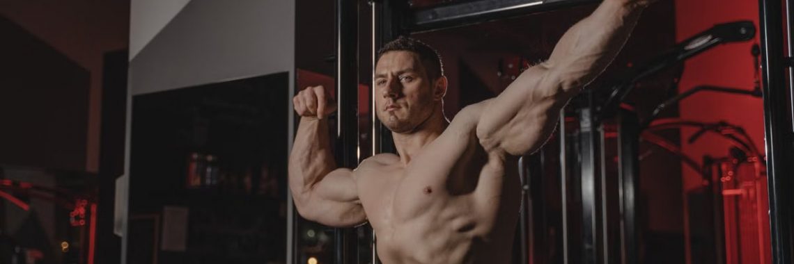 Strong and muscular man posing topless in a gym, showcasing fitness and strength.